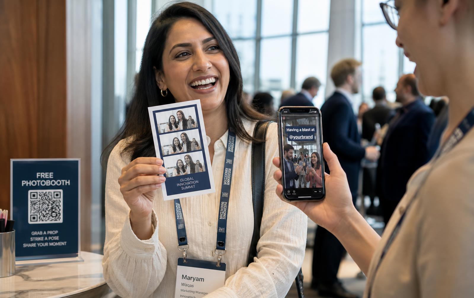 A delegate at the coffee break holding the event photo card while a colleague shows the clip on her phone